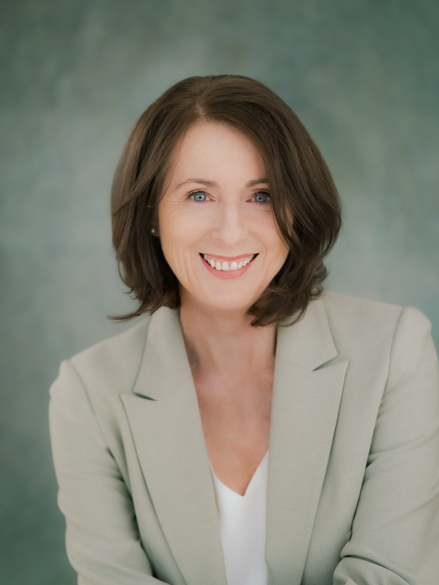 Business headshot of a Brisbane professional woman against a teal background.